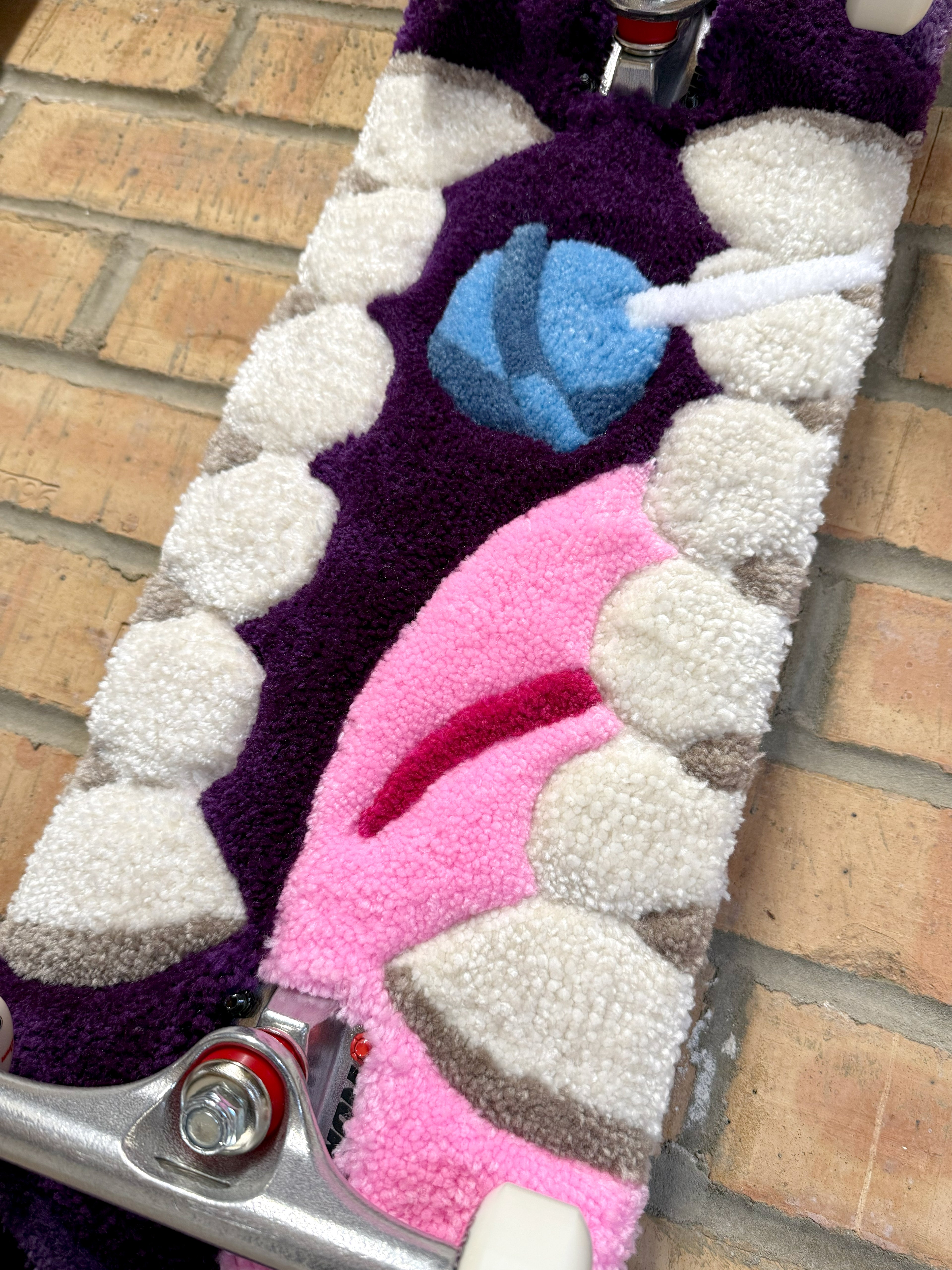 Close-up of the Bad Mouth Rugboard featuring a handmade tufted mouth design with white teeth, pink tongue and blue lollipop mounted on a skateboard deck.