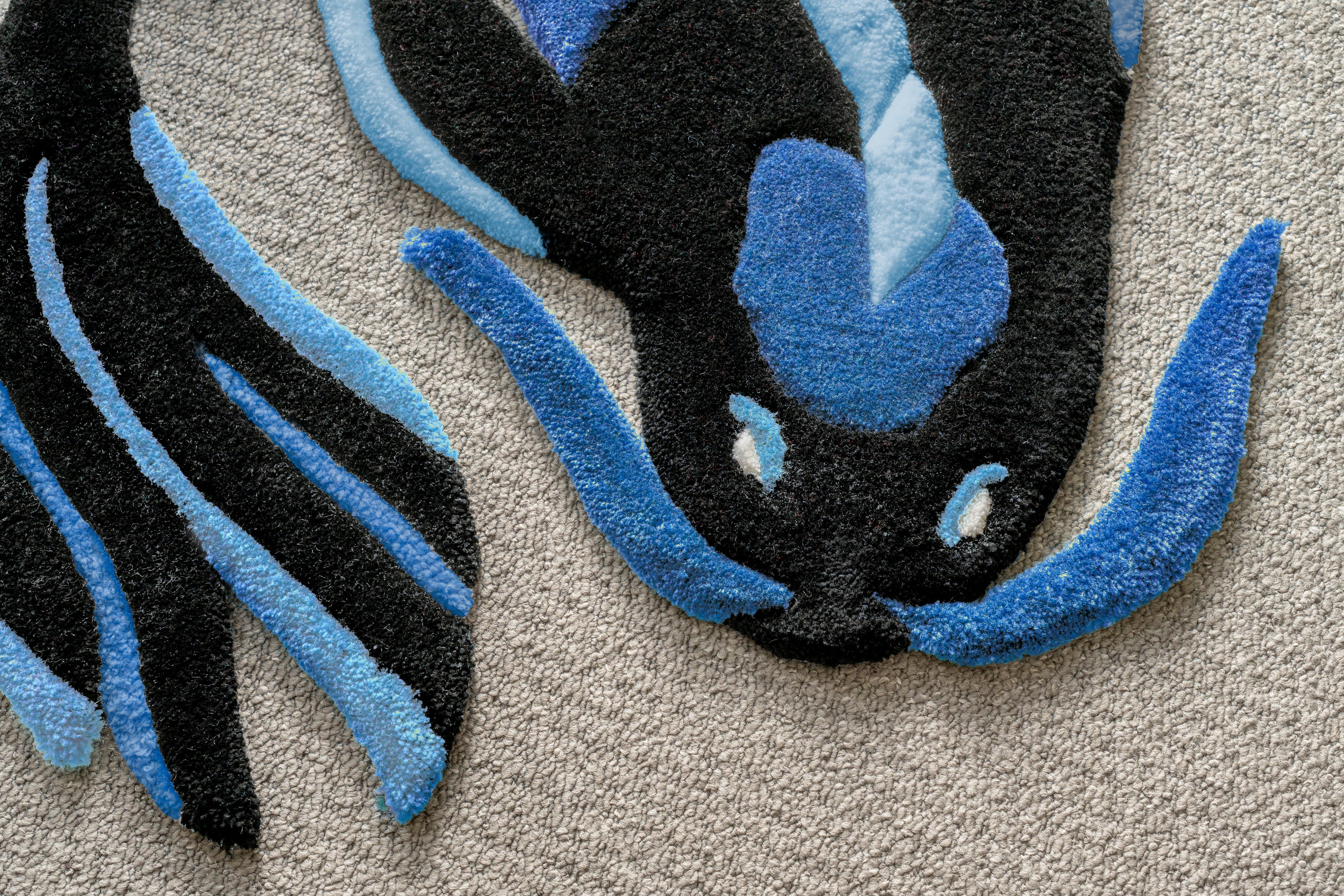 Close-up of a handmade blue koi fish rug showing detailed tufting, sculpted edges and contrasting blue accents.
