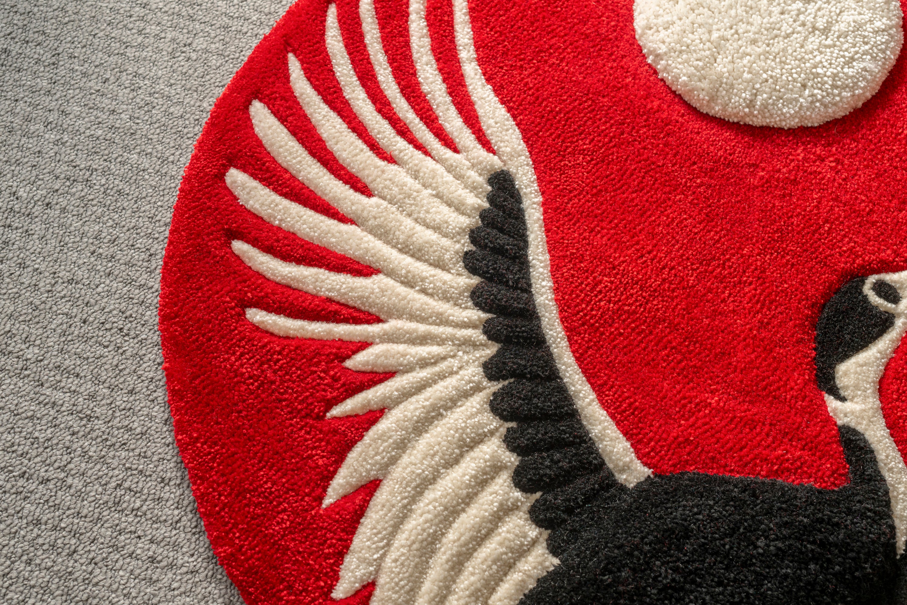 Close-up of the crane wing feathers on a handmade Japanese crane rug with textured tufting and striking red backdrop.