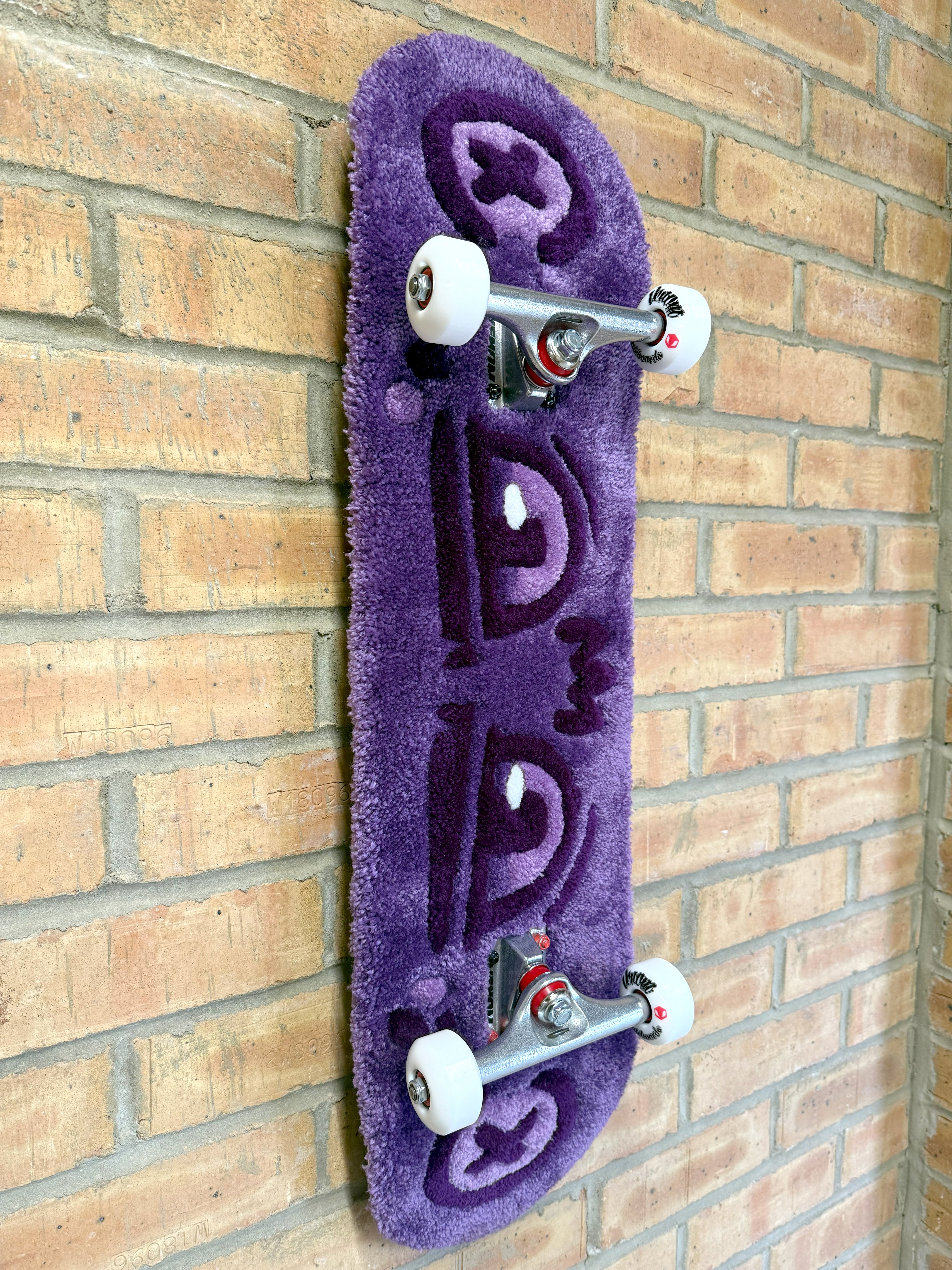 Angled view of the Dirty Look Rugboard showcasing the dimensional tufted artwork, purple eye motif and skateboard deck profile.