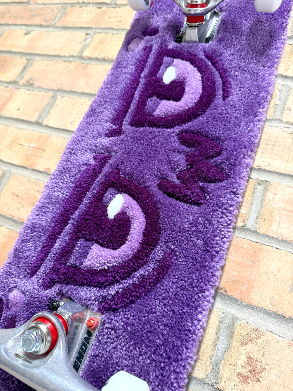 Close-up of the Dirty Look Rugboard featuring a handmade tufted purple eye design mounted on a skateboard deck with trucks and wheels.