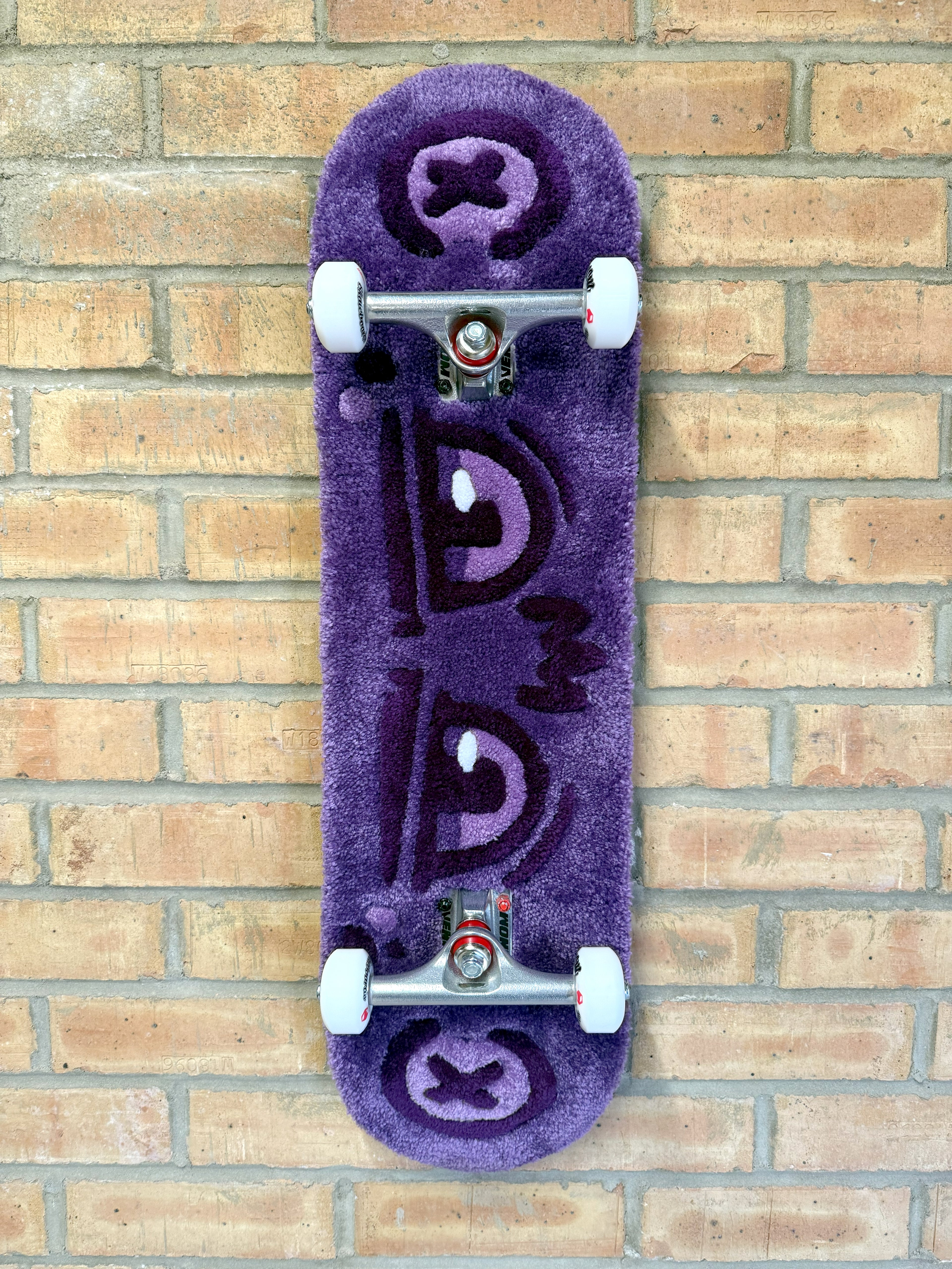 Full view of the Dirty Look Rugboard featuring a purple tufted eye design mounted on a complete skateboard deck with trucks and wheels.