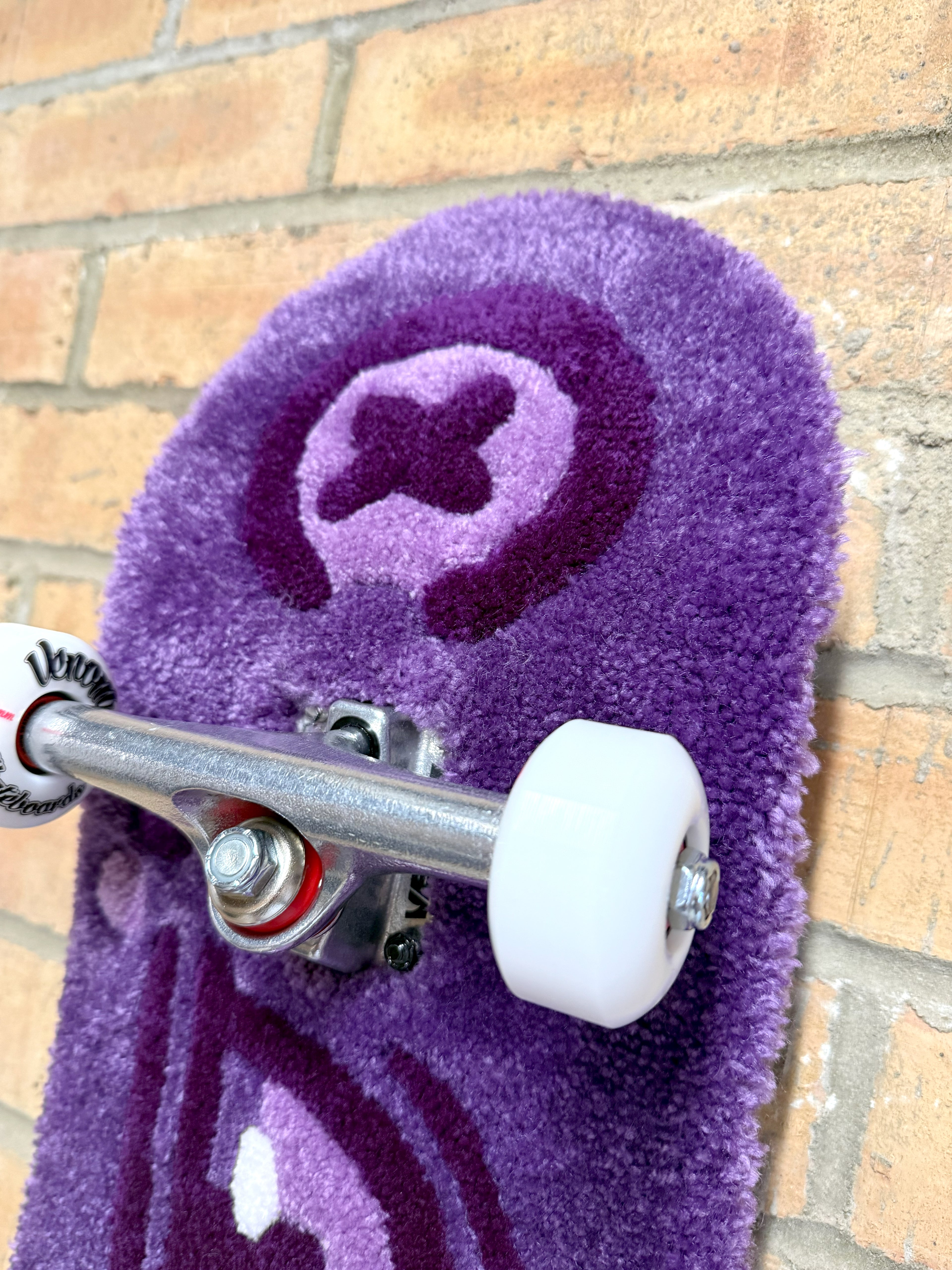 Detailed view of the top section of the Dirty Look Rugboard showcasing the tufted eye graphic, layered texture and skateboard hardware.