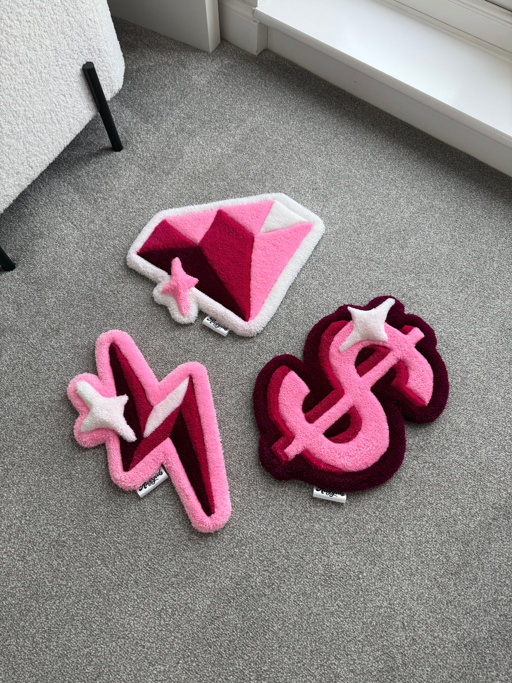 Pink handmade tufted rugs featuring a diamond, dollar sign and lightning bolt design arranged on a light grey carpet.