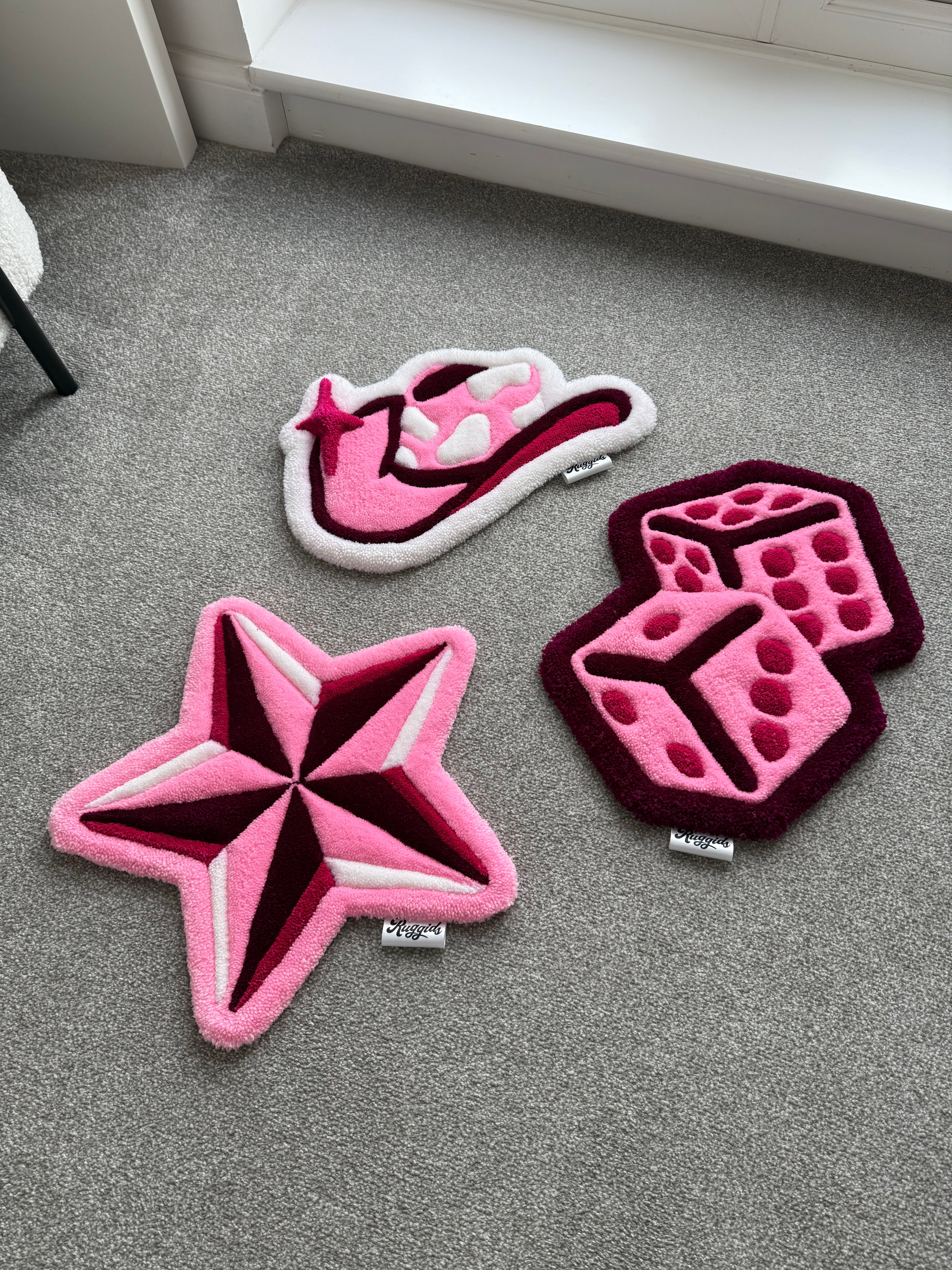 Handmade tufted rug collection featuring pink dice, star and cowgirl boot designs displayed together on a carpeted floor.