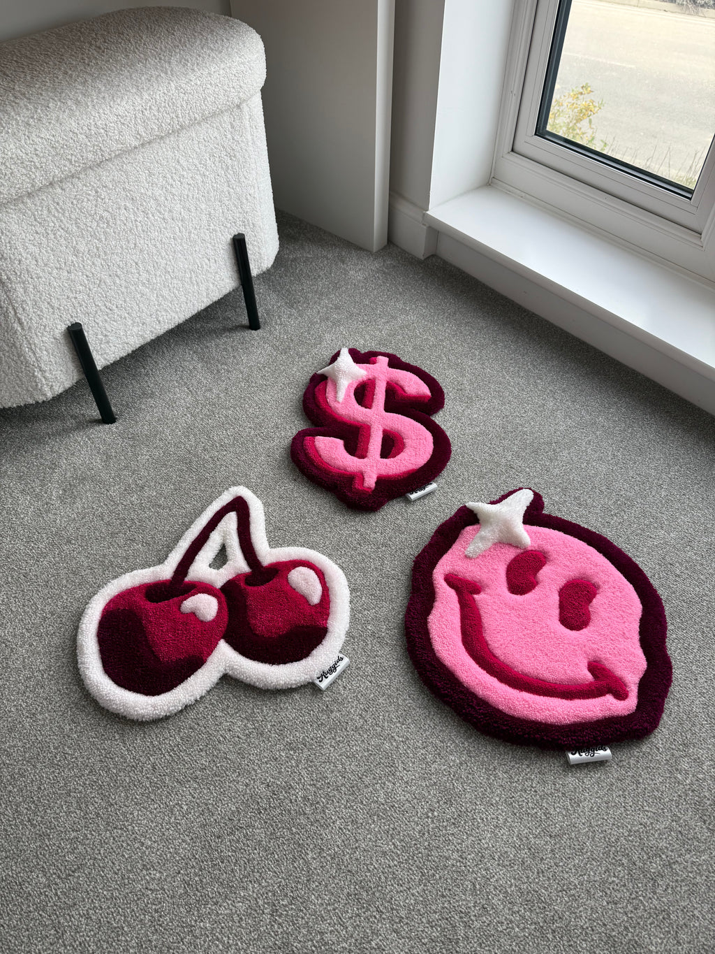 Handmade tufted rug collection featuring a pink smiley face, dollar sign and cherry design displayed together in a modern room.