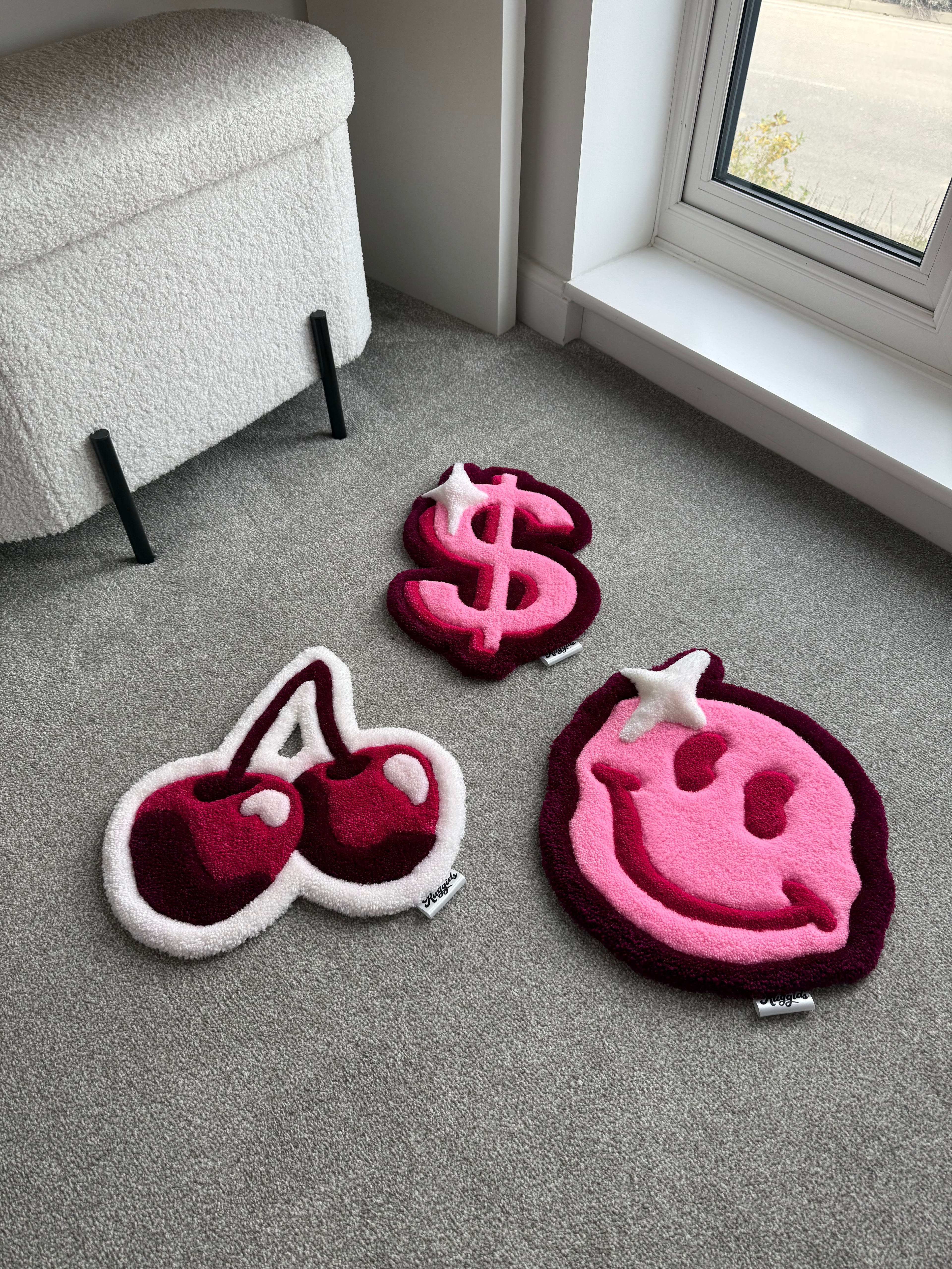 Handmade tufted rug collection featuring a pink smiley face, dollar sign and cherry design displayed together in a modern room.