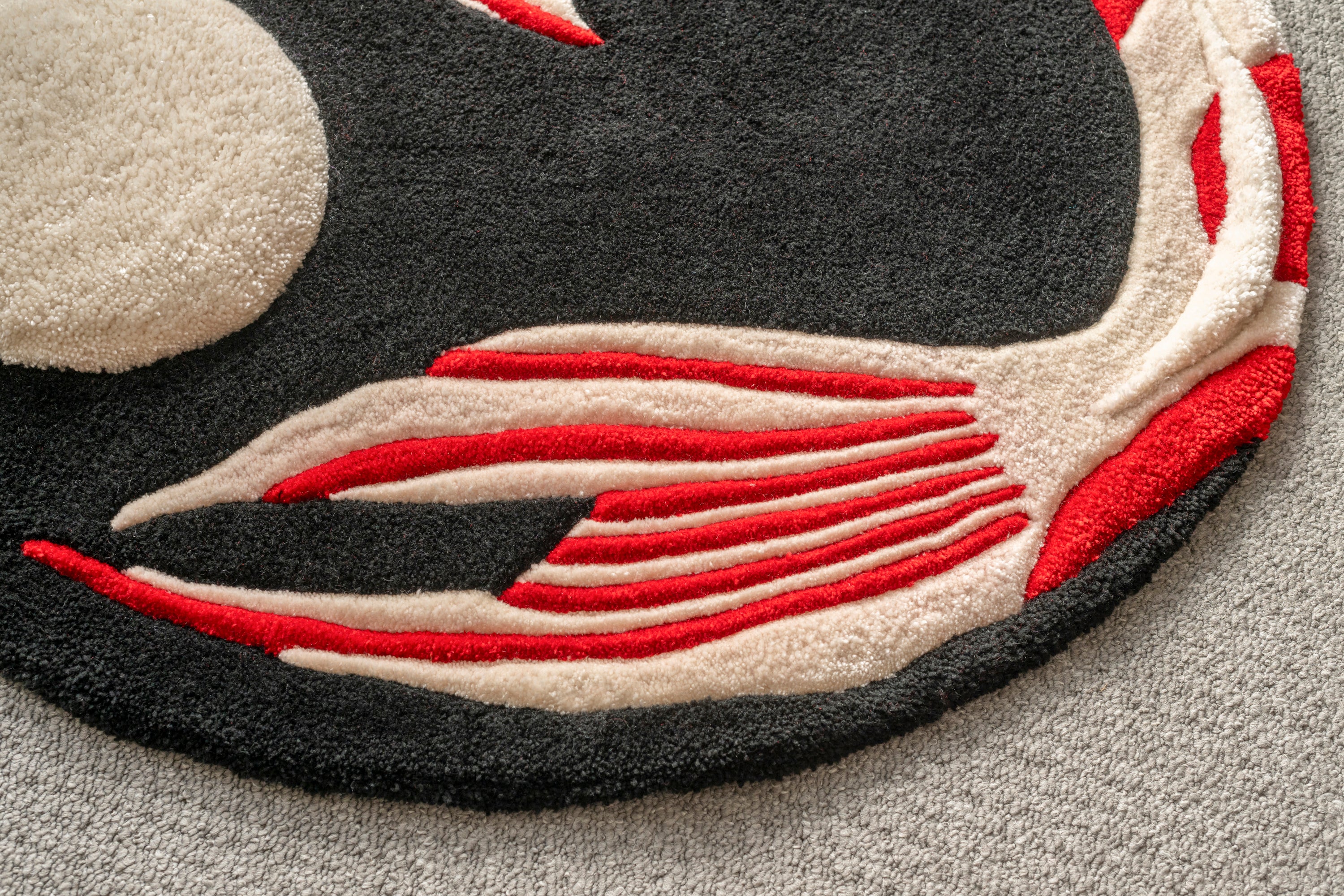 Detailed view of the flowing koi tail on a handmade koi fish rug featuring red, cream and black tones.