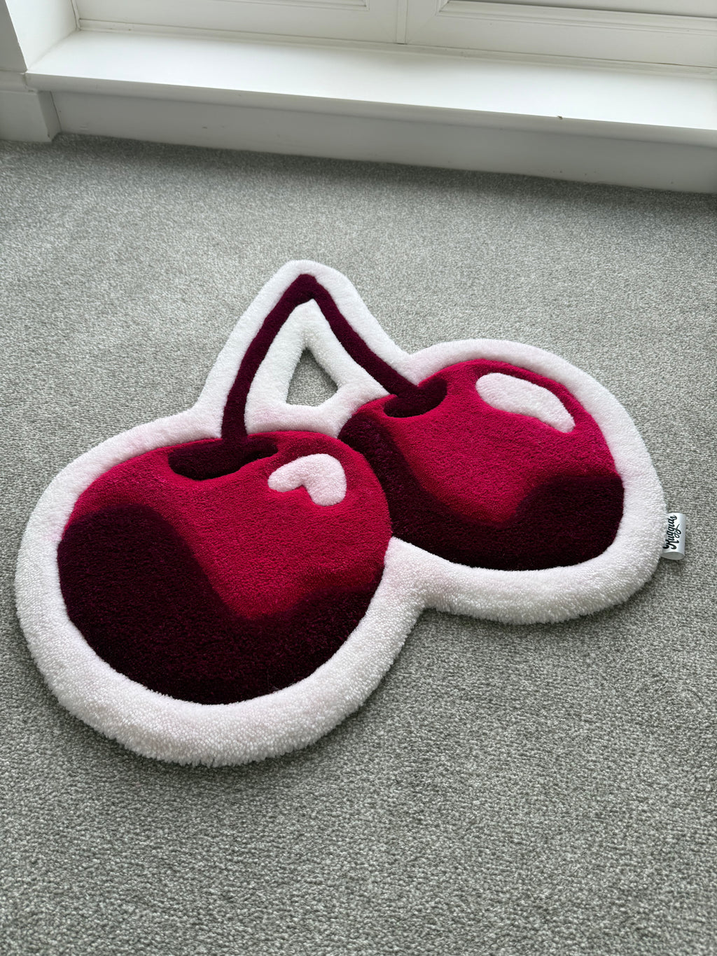 Angled view of a handmade pink cherry rug showcasing its sculpted shape, soft acrylic yarn and layered tufted details.