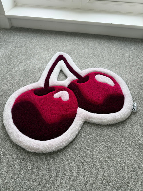 Angled view of a handmade pink cherry rug showcasing its sculpted shape, soft acrylic yarn and layered tufted details.