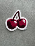 Handmade pink cherry rug featuring two glossy cherries in pink, burgundy and white with a soft low-pile finish.
