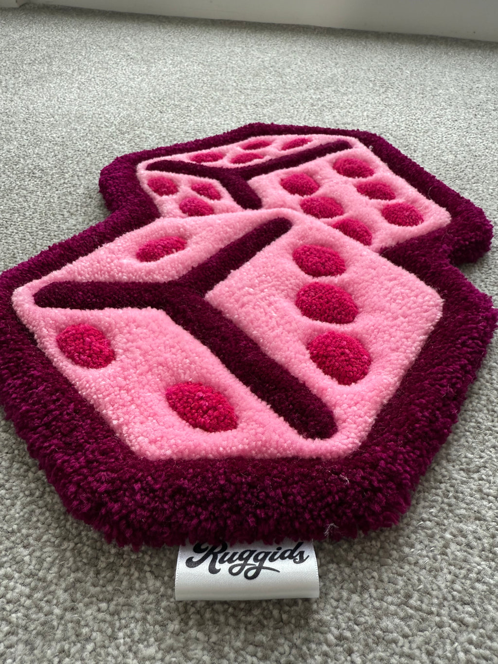 Angled view of the handmade pink dice rug highlighting its layered design, bold outline and handcrafted tufted construction.