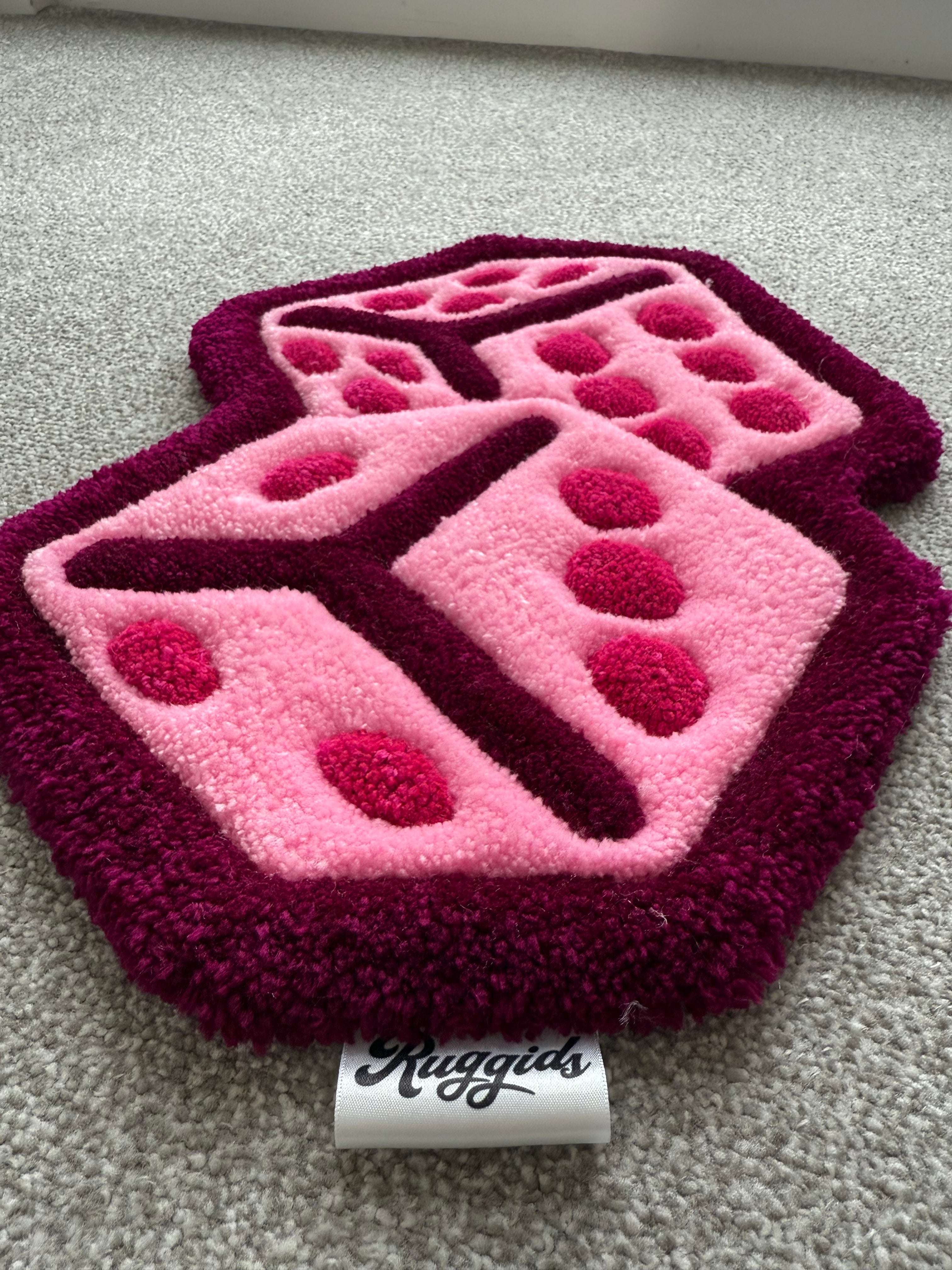 Angled view of the handmade pink dice rug highlighting its layered design, bold outline and handcrafted tufted construction.
