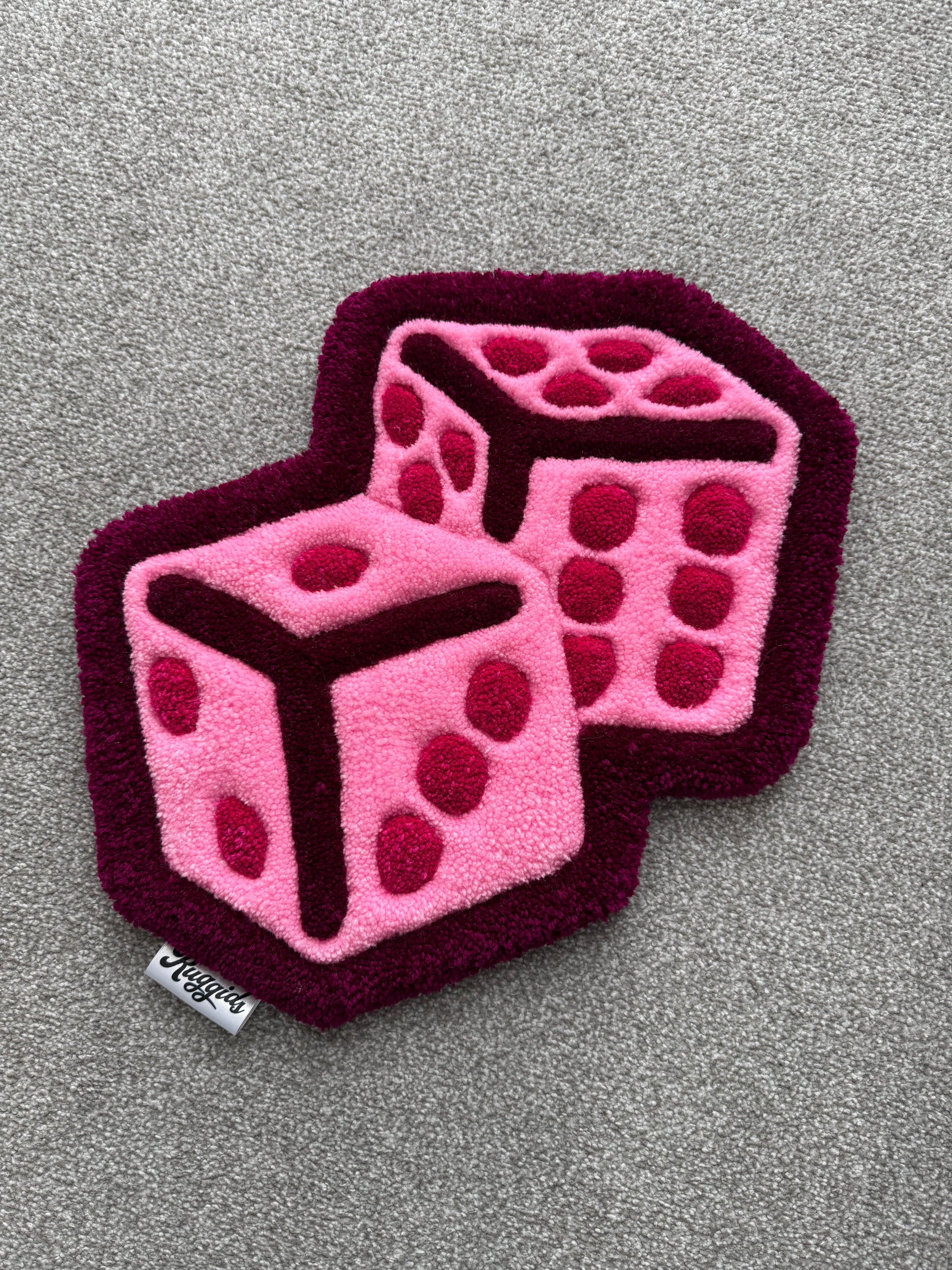 Handmade pink dice rug featuring two overlapping dice in shades of pink with a burgundy outline and low-pile tufted finish.