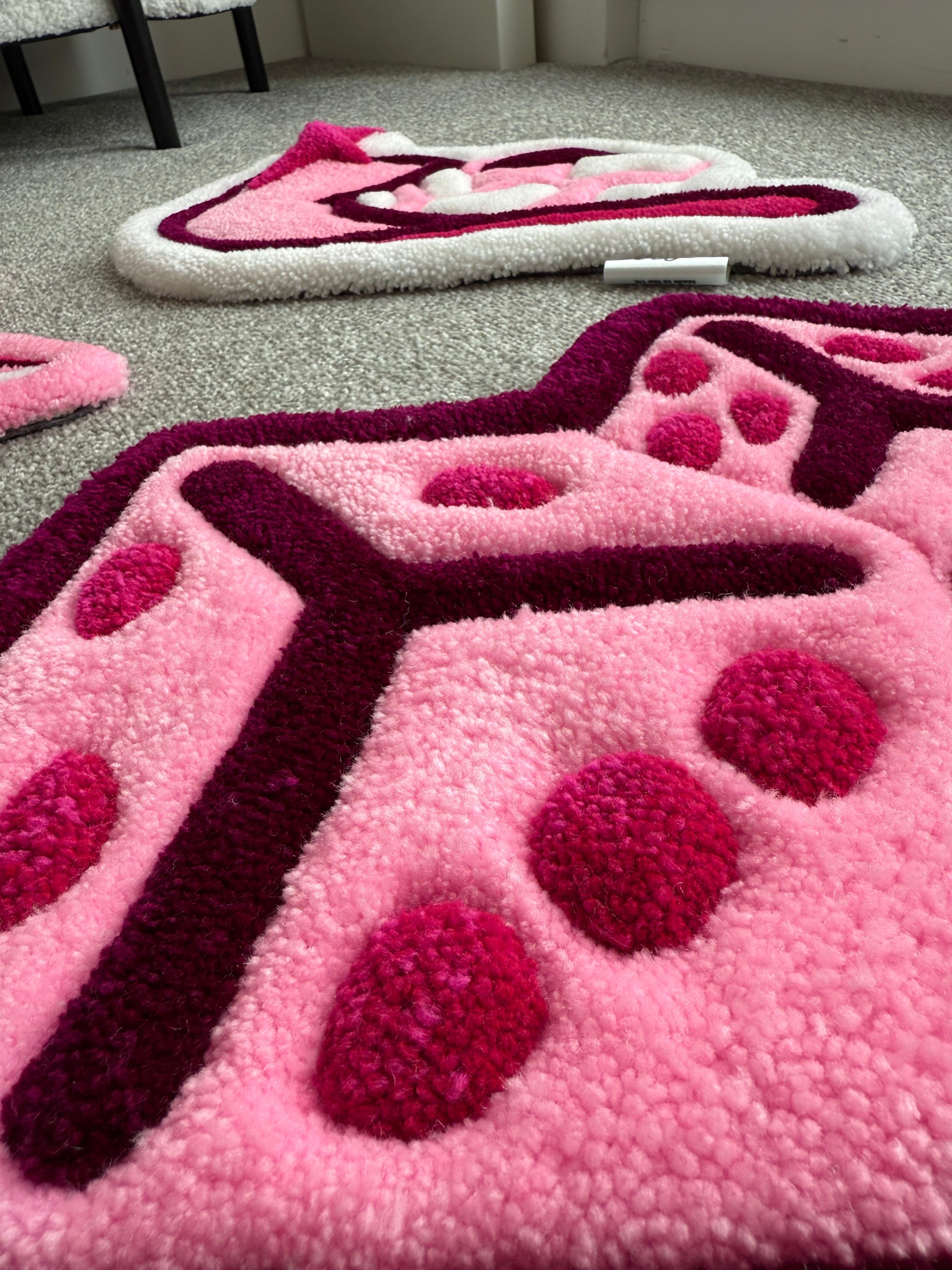 Low-angle view of the handmade pink dice rug showcasing its low-pile tufted texture, dimensional details and soft acrylic yarn finish.