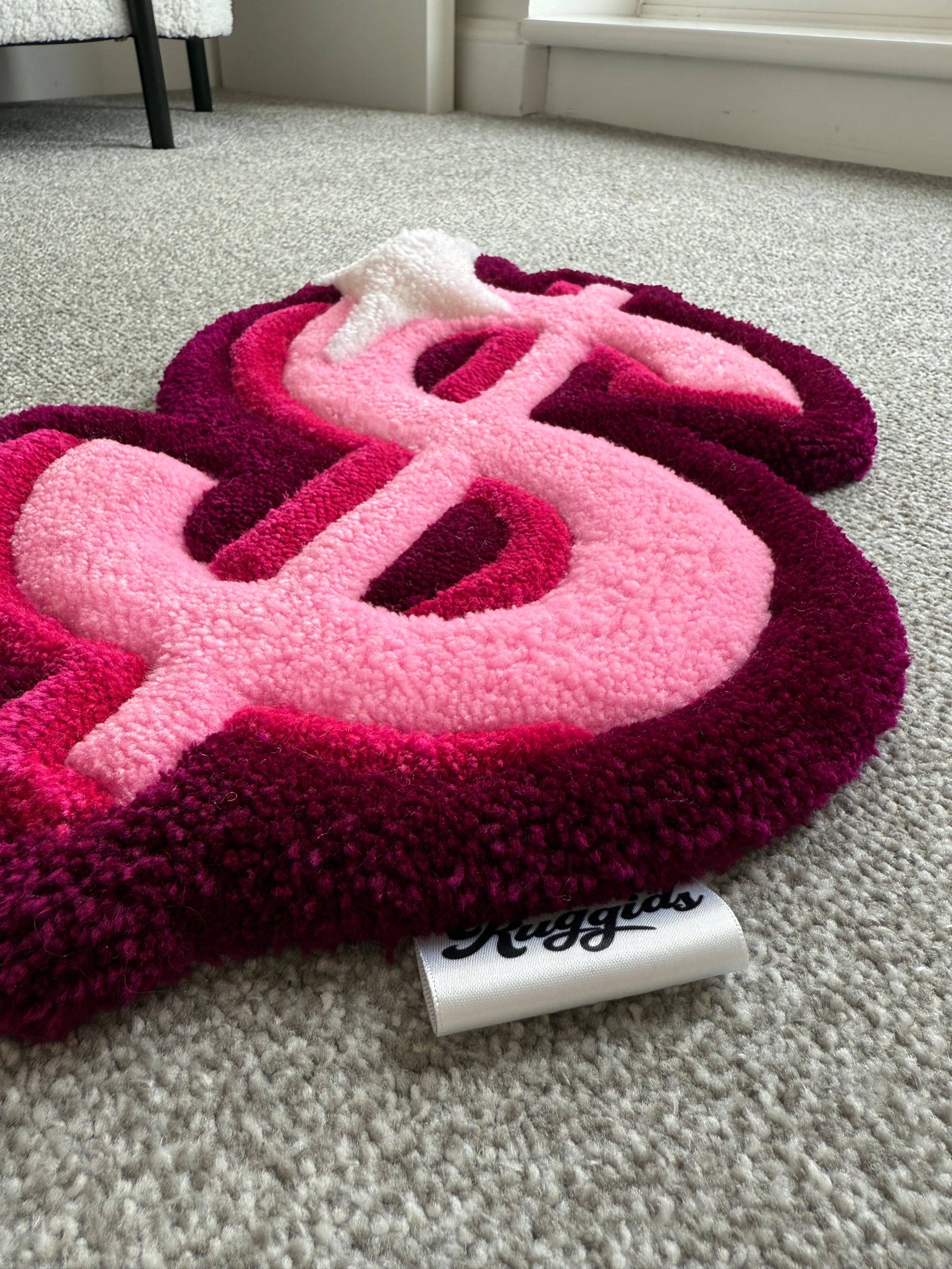 Angled view of a pink dollar sign rug showcasing dimensional tufting, soft acrylic yarn and handcrafted detailing.