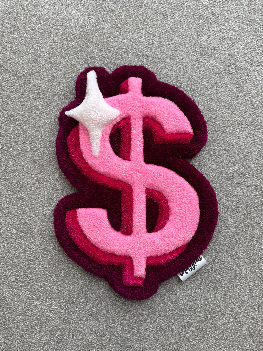 Handmade pink dollar sign rug featuring layered pink tones, burgundy accents and a white sparkle detail with a low-pile tufted finish.