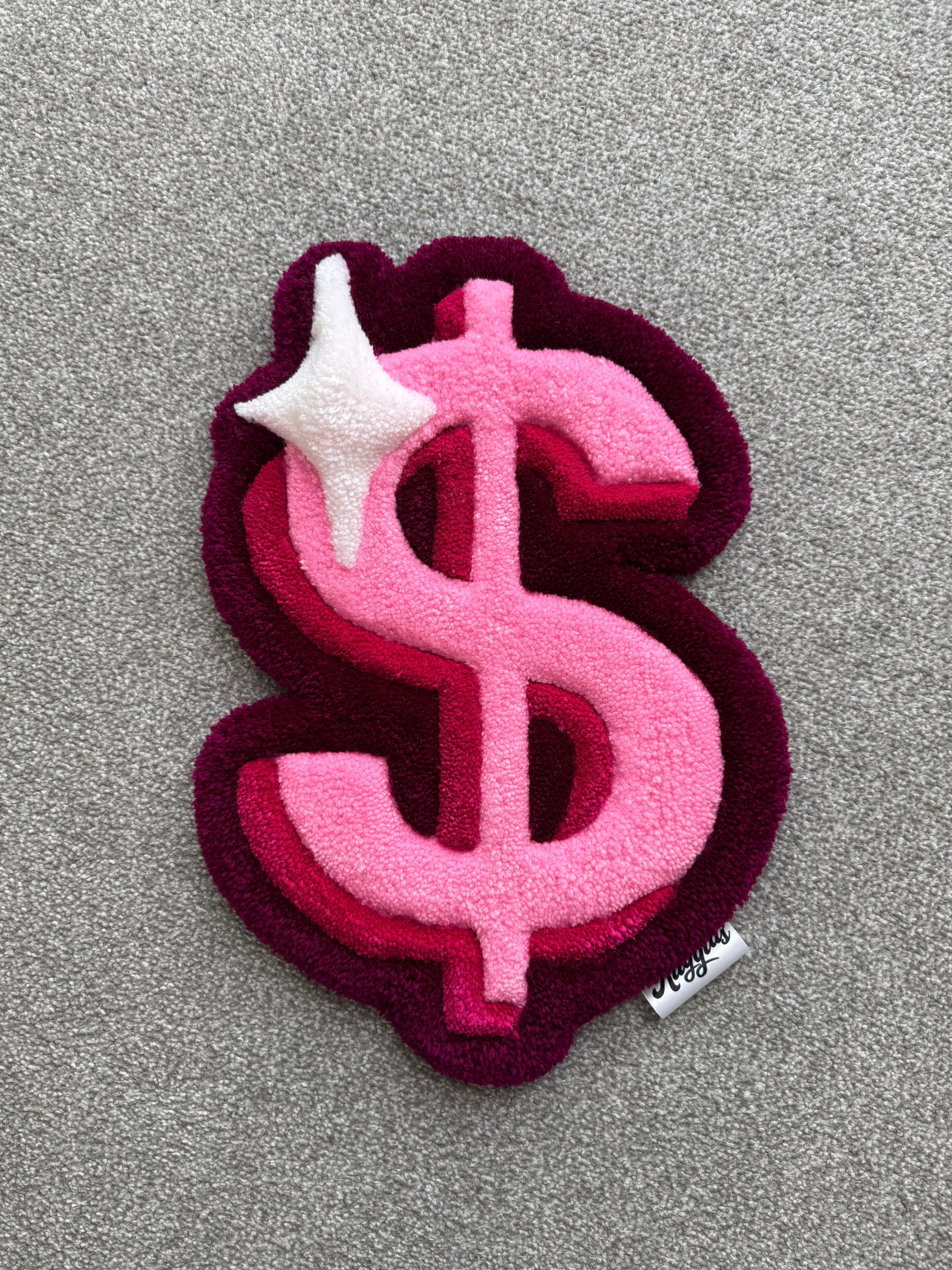 Handmade pink dollar sign rug featuring layered pink tones, burgundy accents and a white sparkle detail with a low-pile tufted finish.