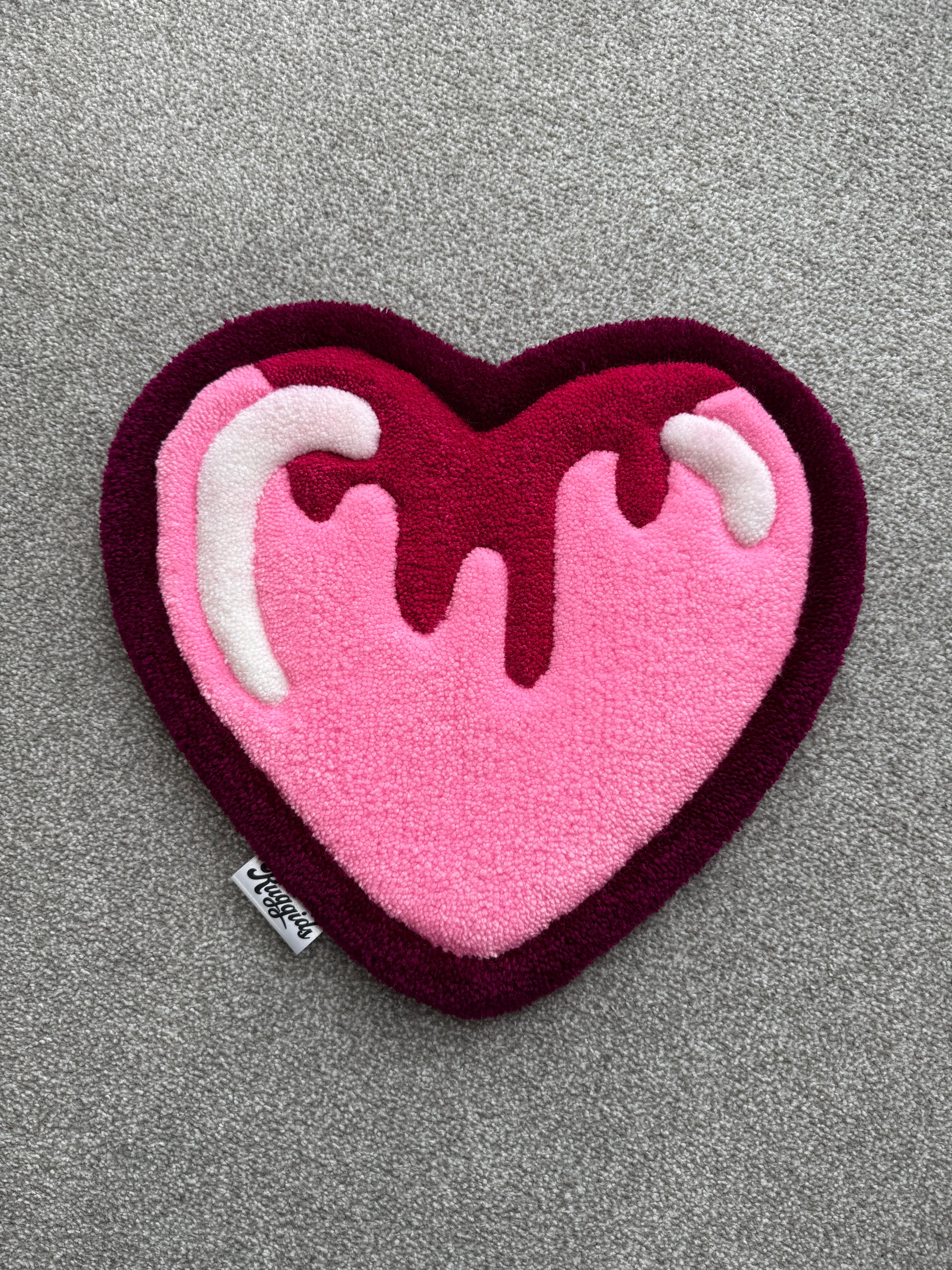 Handmade pink heart rug featuring a dripping icing-inspired design in shades of pink, burgundy and white with a low-pile tufted finish.