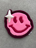 Handmade pink smiley face rug featuring a playful smiling face design with a white sparkle accent and low-pile tufted finish.