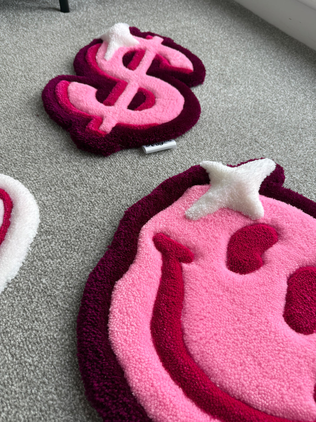 Lifestyle view of the handmade pink smiley face rug alongside matching tufted rugs from the For The Girls collection.