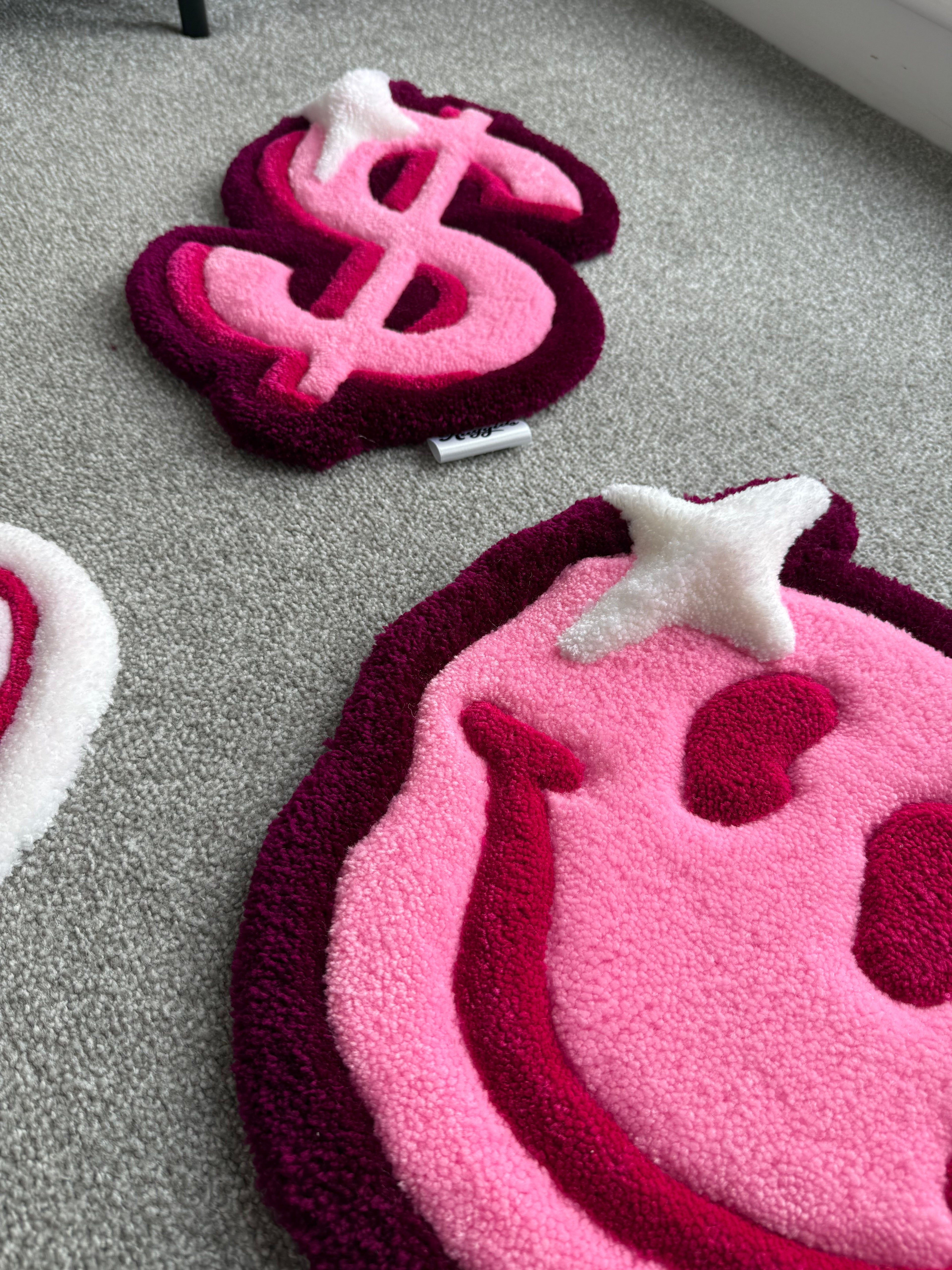 Lifestyle view of the handmade pink smiley face rug alongside matching tufted rugs from the For The Girls collection.