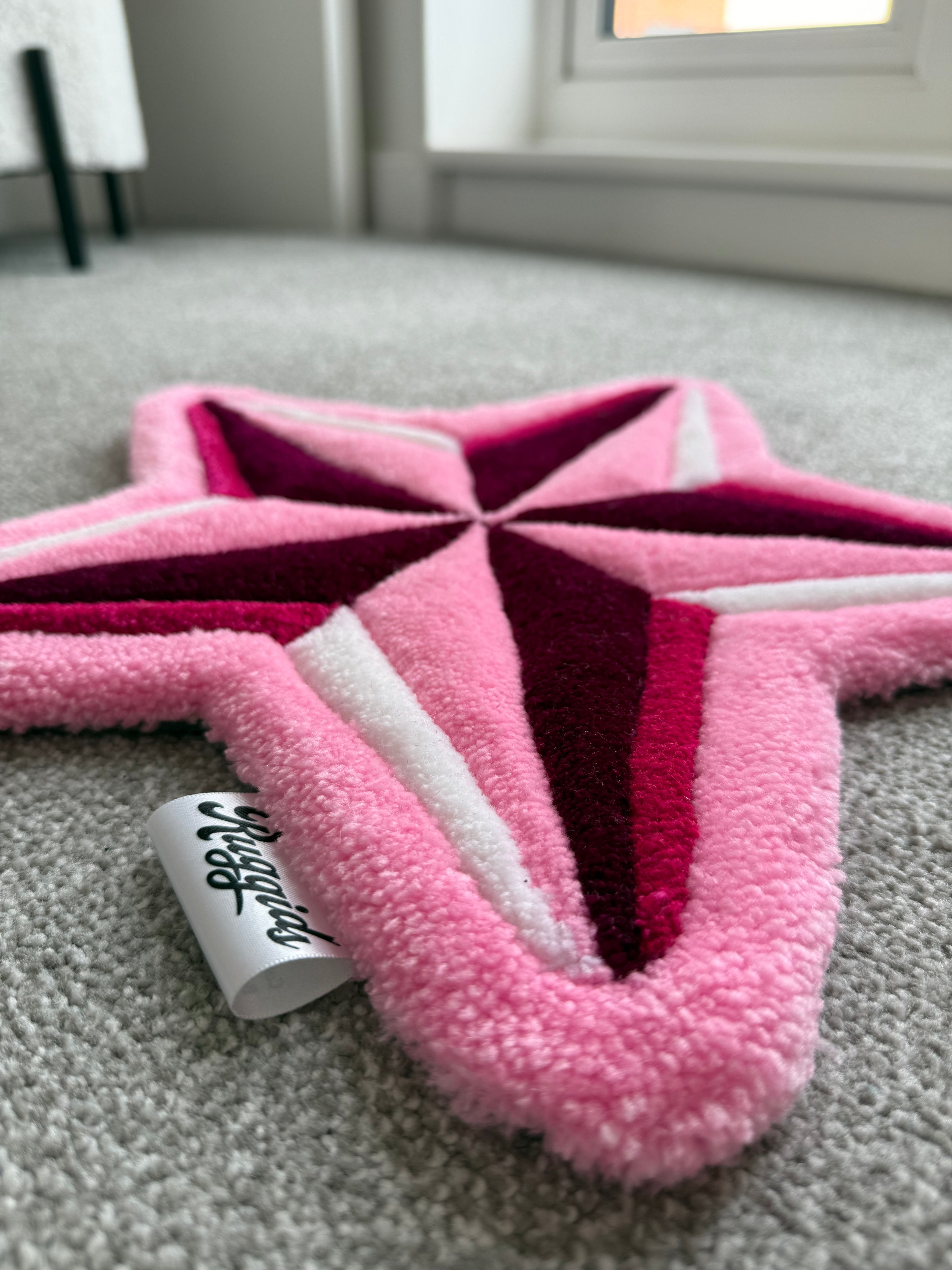 Low-angle view of a handmade pink star rug showcasing its low-pile tufted texture and dimensional design.