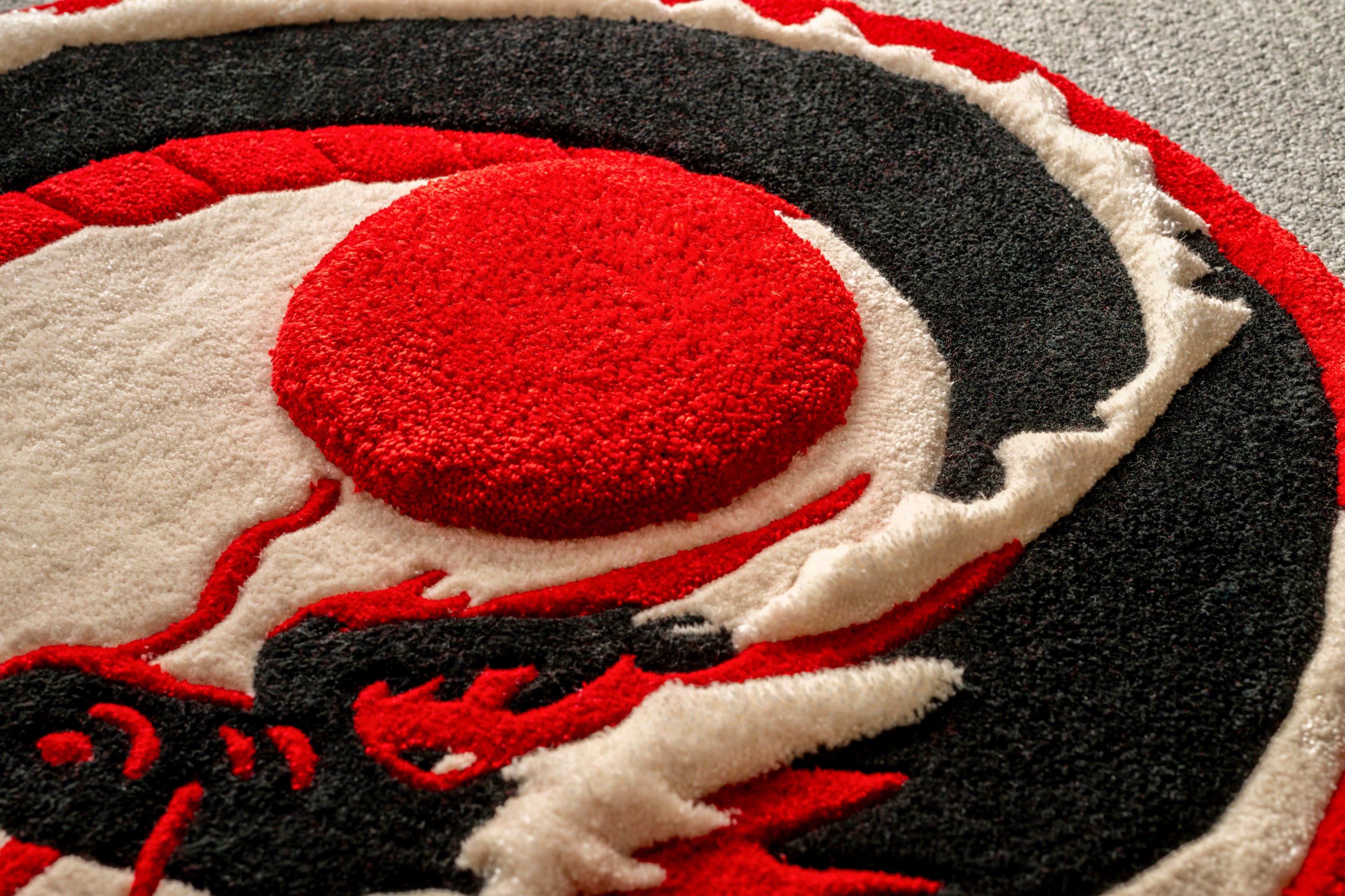 Detailed texture shot of the raised red sun and surrounding dragon artwork on a handmade tufted rug.