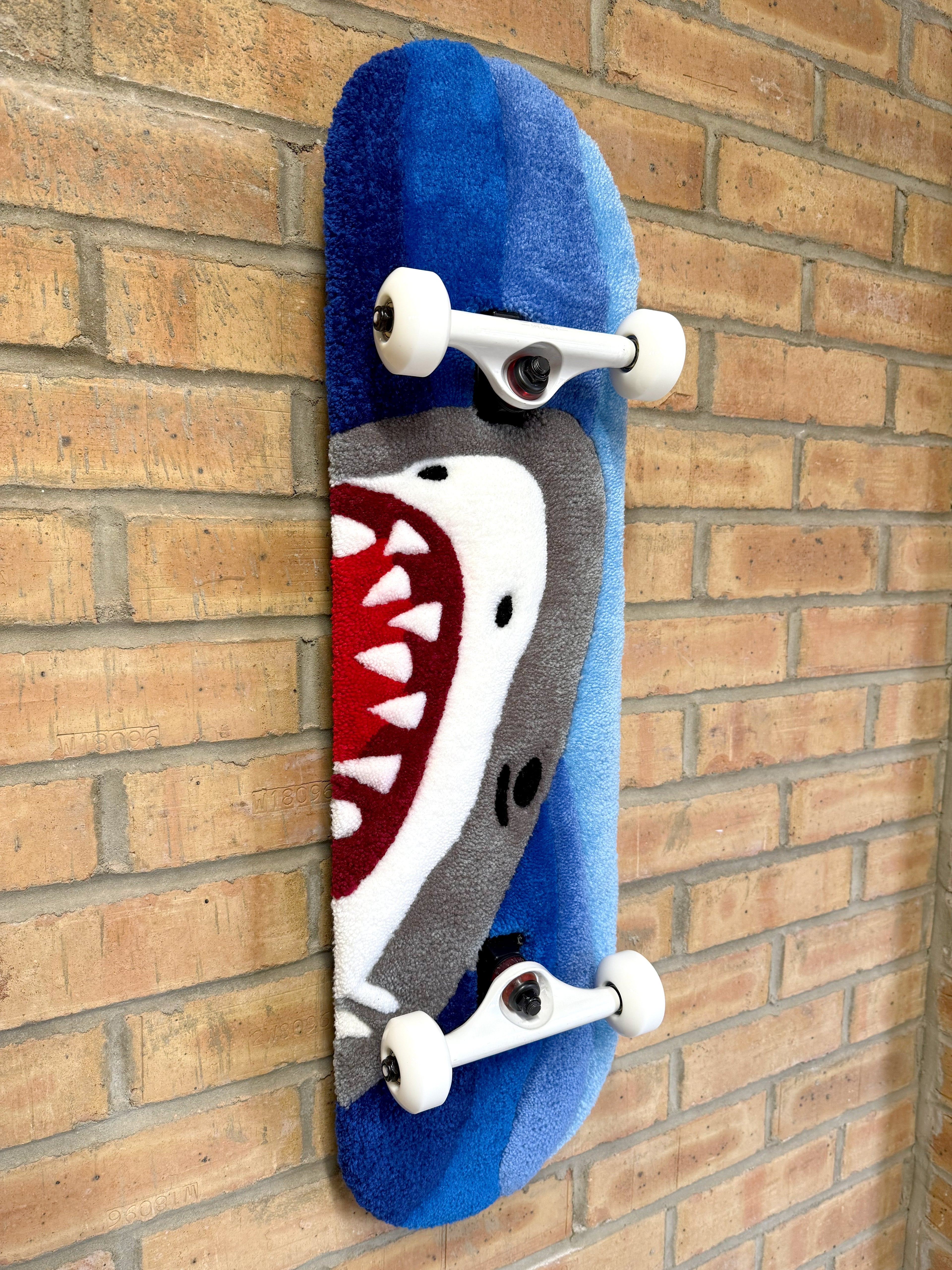 Angled view of the Shark Rugboard displaying the shark design, blue wave pattern, and skateboard deck profile