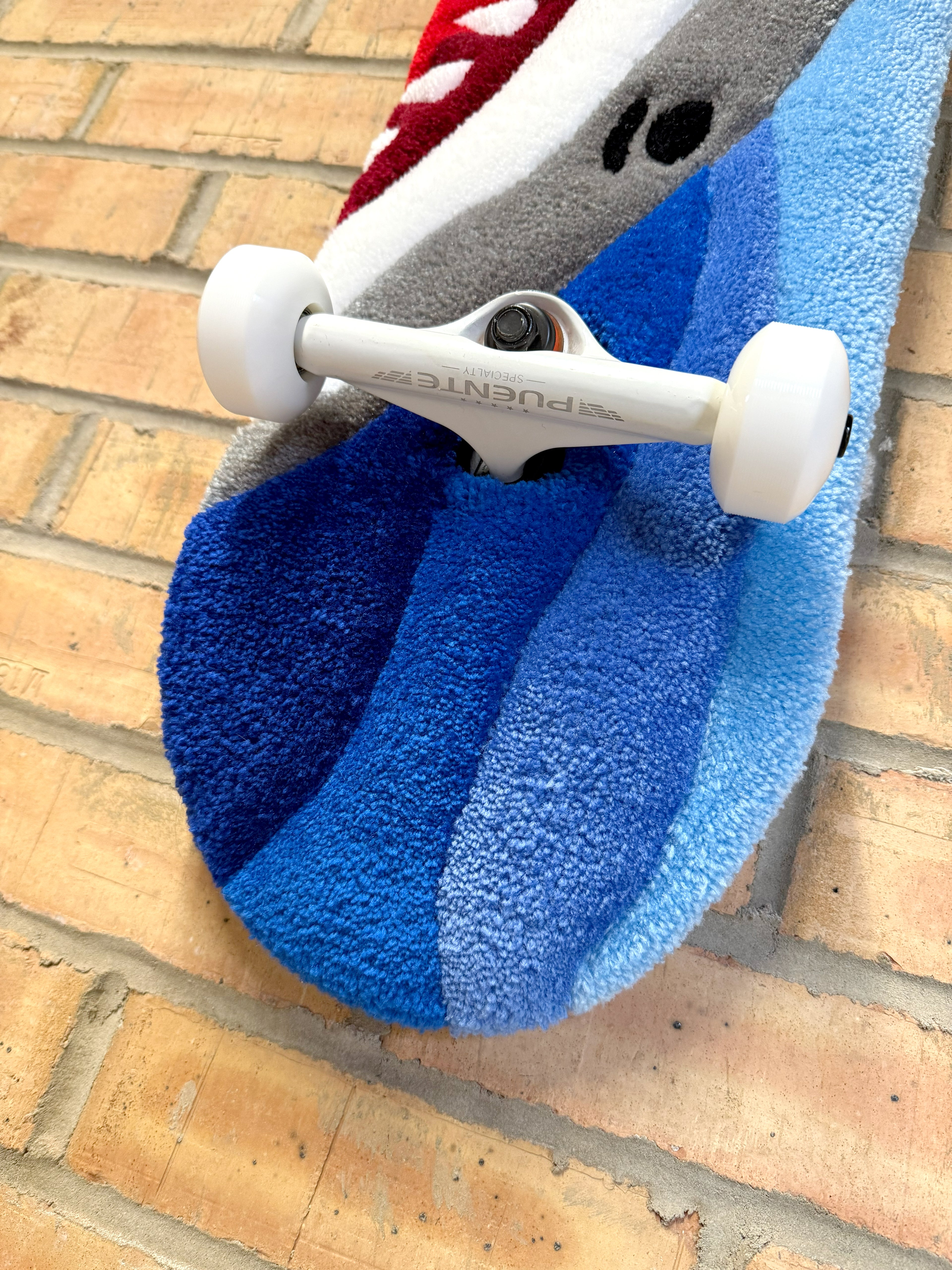 Detailed view of the Shark Rugboard highlighting layered blue tufting, skateboard hardware, and ocean-inspired design